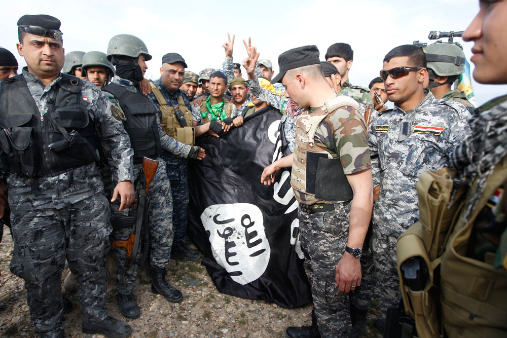 Homens da polícia iraquiana e combatentes xiitas seguram uma bandeira Estado Islâmico. (Foto: REUTERS/THAIER AL-SUDANI)