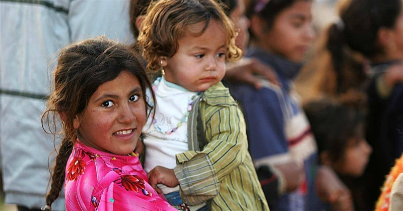 Garota síria segura bebê no colo, em campo de refugiados. 