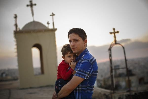 Homem cristão segurando seu filho, enquanto muitos de seus vizinhos fugiram da violência no Iraque. (Foto: Warrick Page/New York Times)