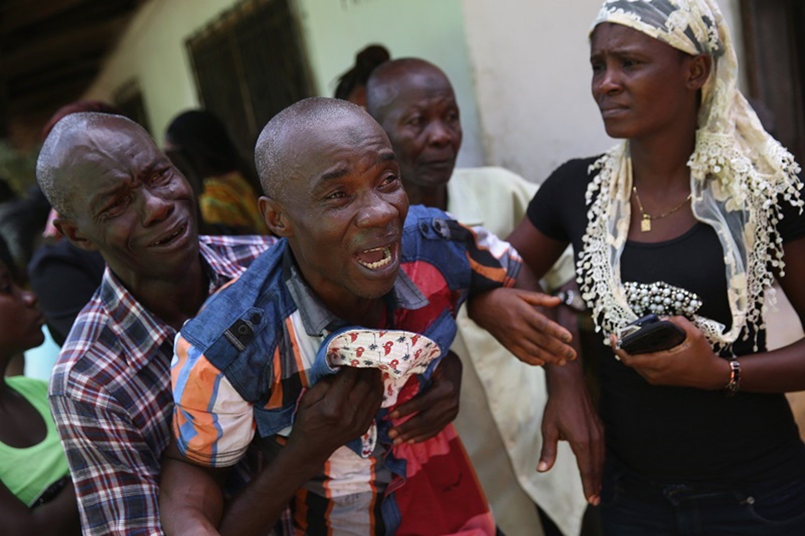 Liberiano chora enquanto o corpo de sua esposa é levado por uma equipe médica na África. (Foto: John Moore/Getty Images)
