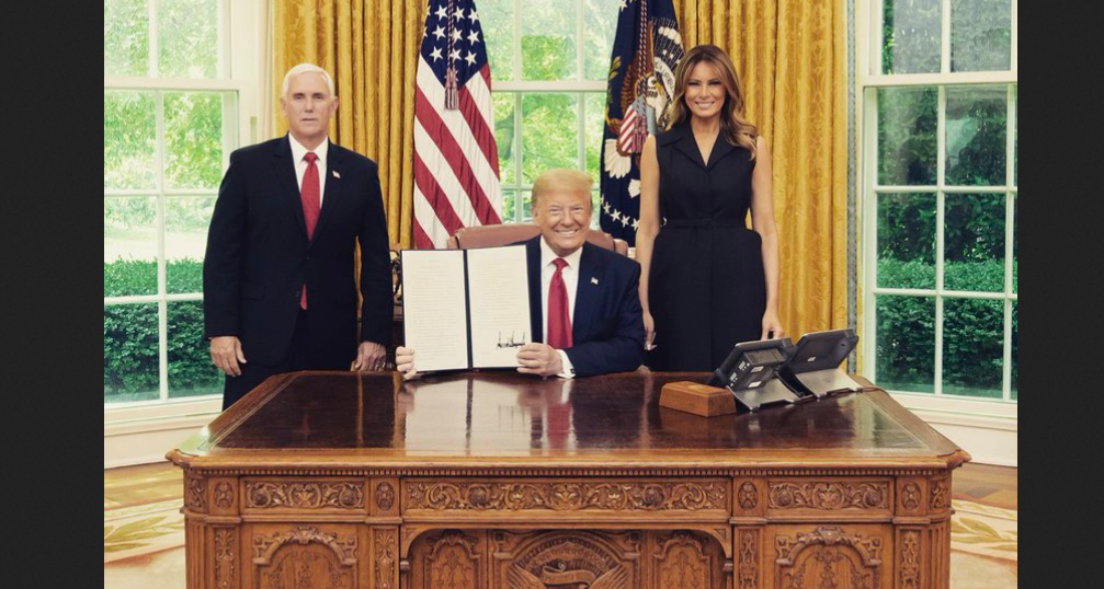 Donald Trump exibe a assinatura da ordem, entre a primeira-dama Melania e o vice Mike Pence. (Foto: Reprodução/Twitter)